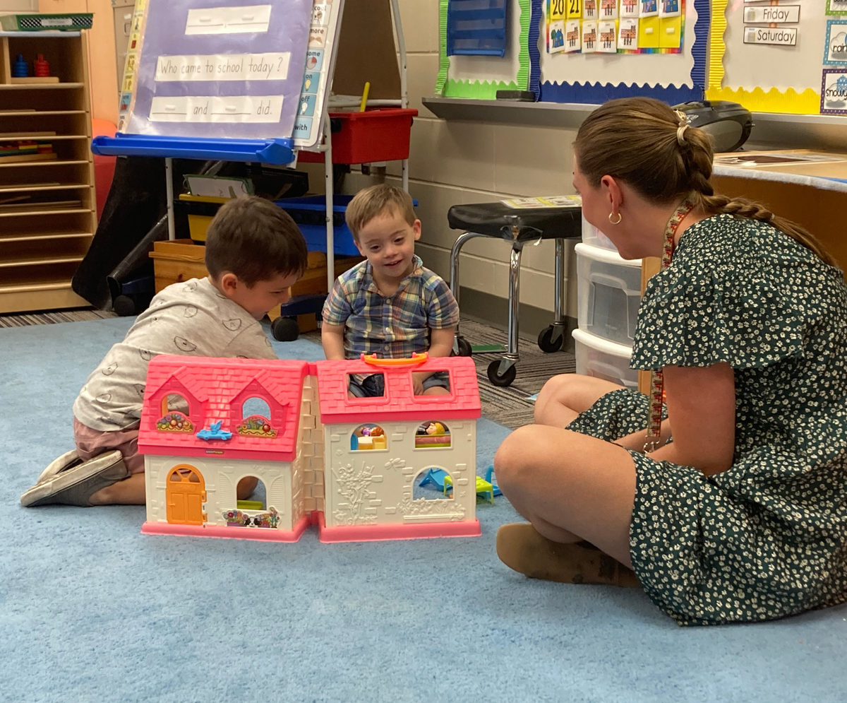 Preschool students playing with toys next to a teacher